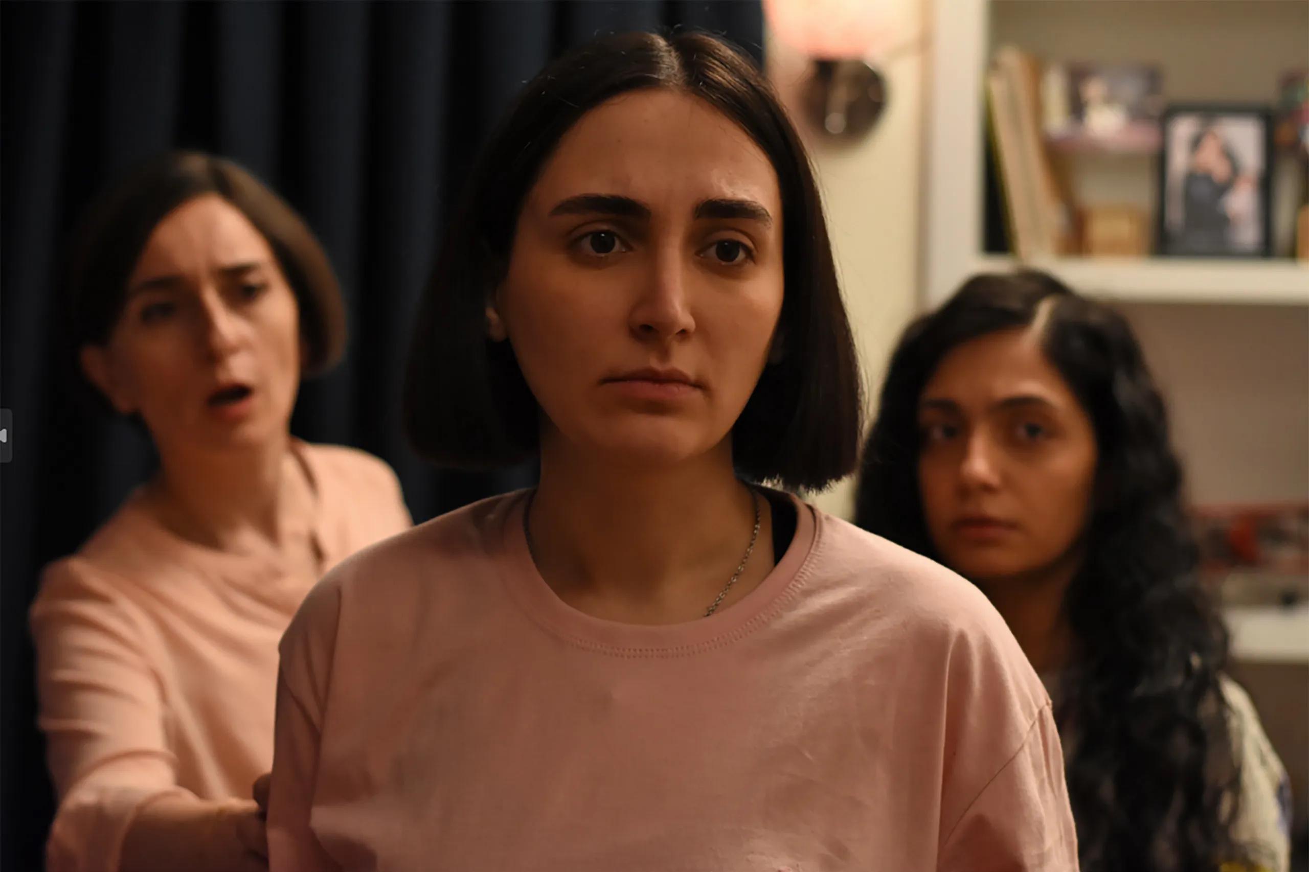 Three women in muted pink clothing stand in a row in a still from The Seed of the Sacred Fig